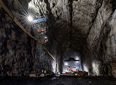 Spotlights illuminate a cavern, scaffolding, construction equipment and workers