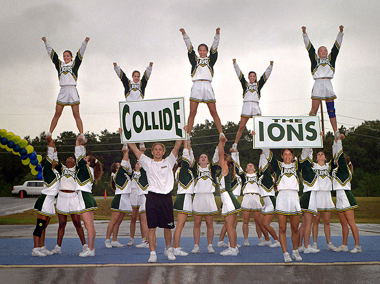Cheerleaders in formation with signs that read Collide Ions