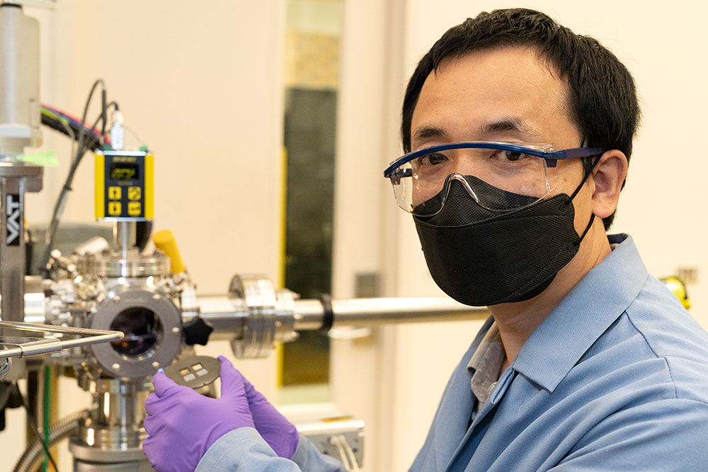 Photo of Mingzhao Liu holding a substrate holder in front of the pulsed laser deposition system