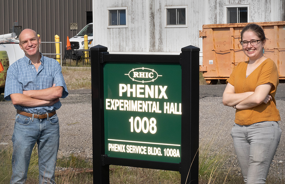 Photo of  Alexander Bazilevsky and Nicole Lewis outside the experimental hall that housed the PHENIX