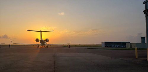 Photo of aircraft facing away from camera on tarmac during orange sunset
