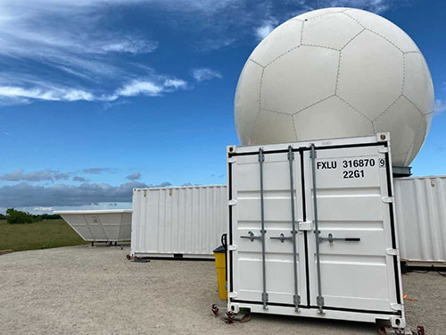 Photo of C-Band ARM Precipitation Radar, a large white sphere atop white shipping containers