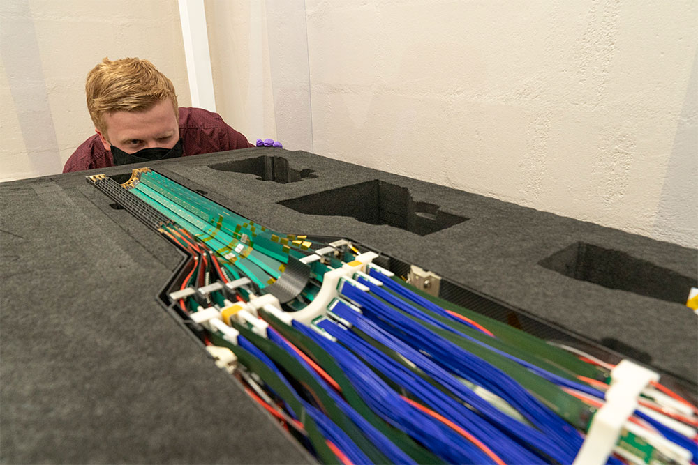Photo of Cameron Dean looking down the barrel of a detector, shown with green sensor strips and line