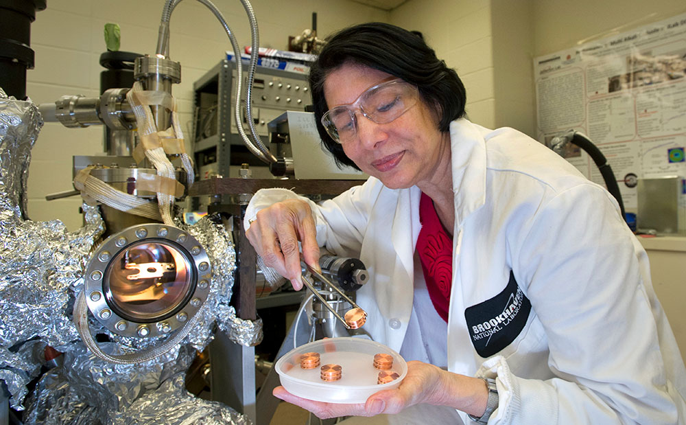 Triveni Rao, wearing clear safety goggles over her eye and a white lab coat with a Brookhaveb Lab lo