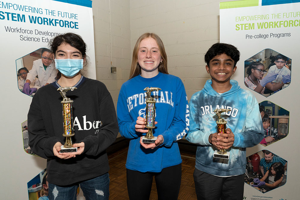 Madison Wolferd, Payton Kelly, and Josiah Koshy pose with sparky trophies topped with a racecar