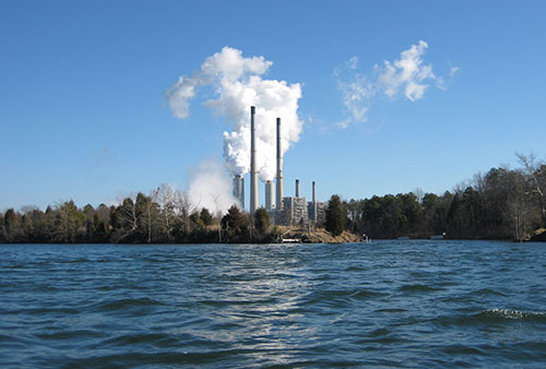 a large  body of water with a power plant and smoke stack on the shore in the distance