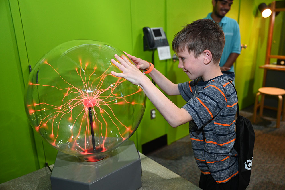 Child hold hands up to on sphere filled with orange streaks of light