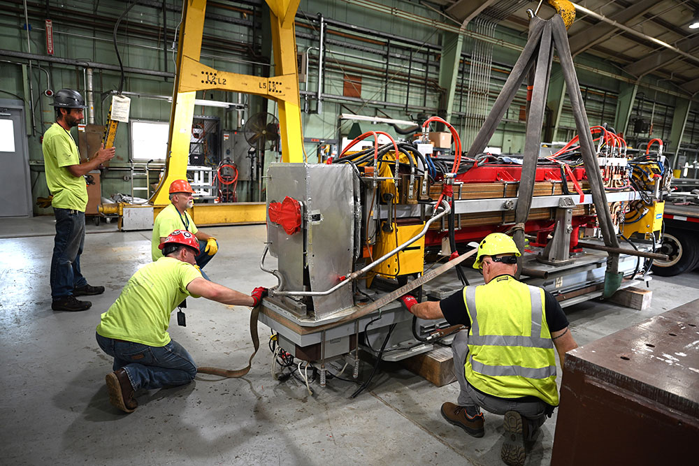 Technicians wearing hardhats and bright yellow shirts rig magnet