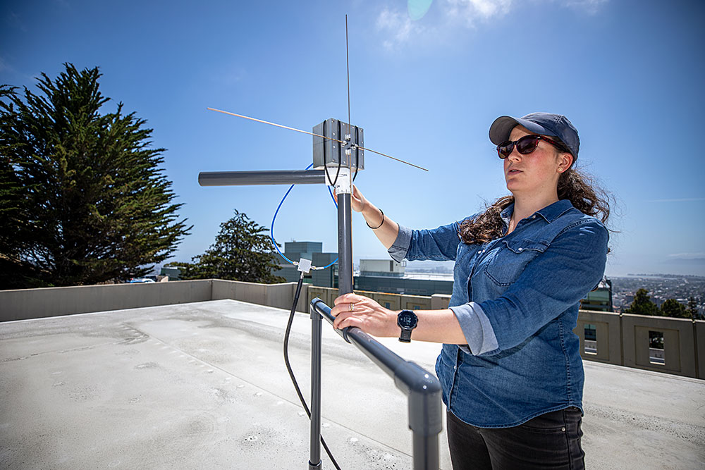 Kaja Rotermund, wearing a blue shirt, baseball cap, and sunglasses, adjusts antenna on a rooftop on