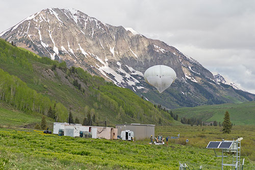 tethered balloon in green field with rocky snow covered mountain in the background