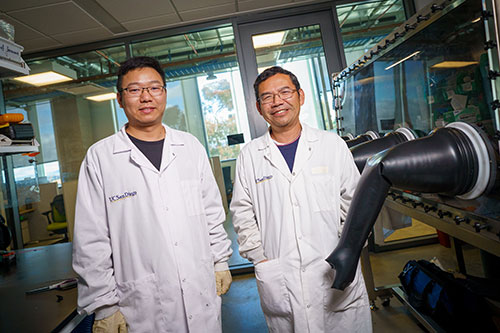 Two scientists in white lab coats standing in a lab.