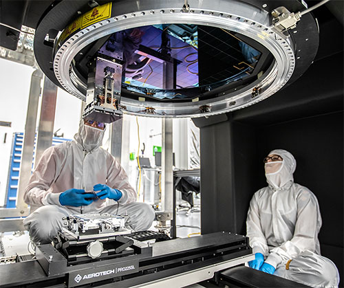 Two scientists wearing PPE look up at large camera lens