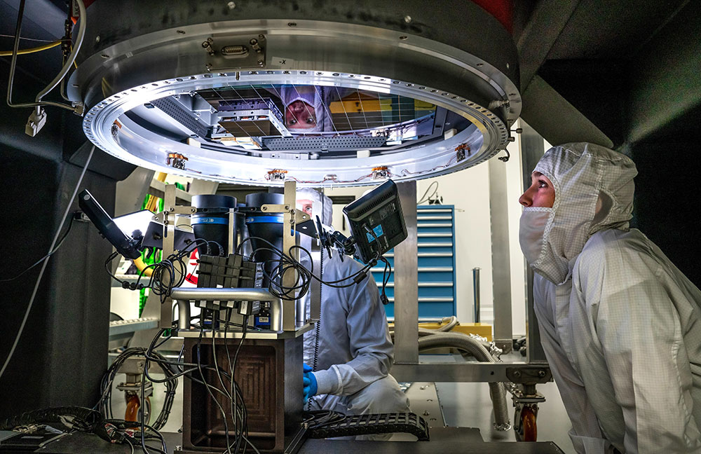 Two scientists wearing PPE look up at large camera lens