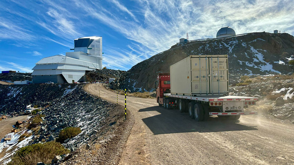 A truck hauling the LSST camera (inside a container) drives up a gravel road towards the Rubin Obser