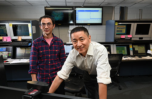 Jiangyong Jia and Shengli Huang with a wall control room monitors behind them