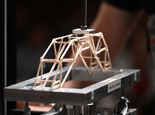 A wooden model bridge sits atop the metal frame of a crashing mahcine