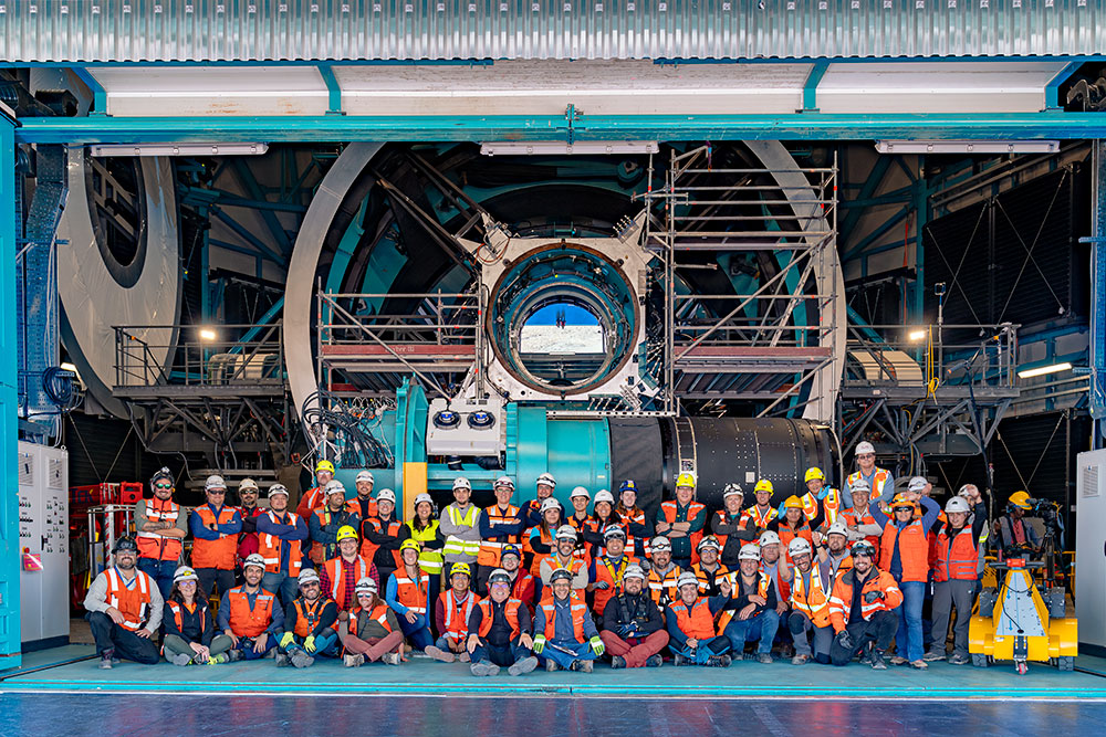 A group of of people where orange safety vests and hard hats pose for a photo in front of the