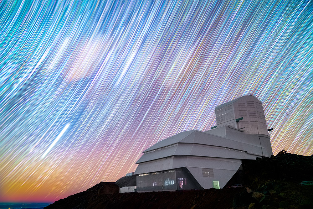 A time-lapse image of the Vera C. Rubin Observatory backed by a blue and purple sky with streaks of