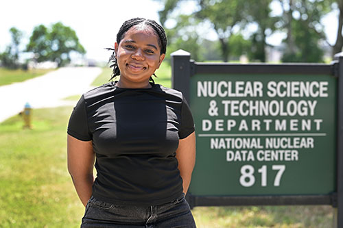Pedrocia De-Sosoo stands smiling in front of a sign for the Nuclear Science & Technology Departm