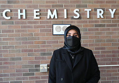 Ieesha Ansar stands in front of a brick wall with "Chemistry" in white, all caps letters