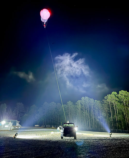 A tethered balloon floats above a research site at night