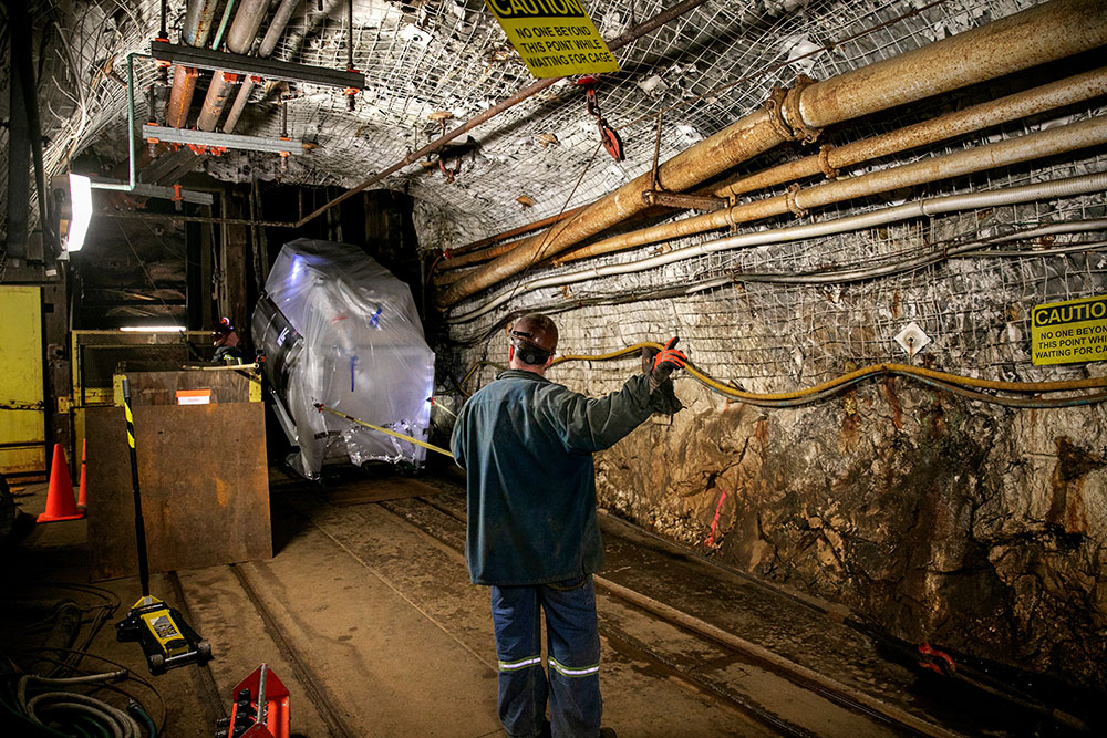 A worker in protective gear maneuvers a large, covered object within a dimly lit underground tunnel.