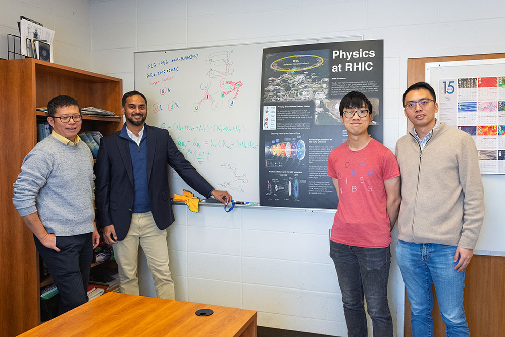 Four physicists stand side by side in an office at Brookhaven National Laboratory during a celebrati
