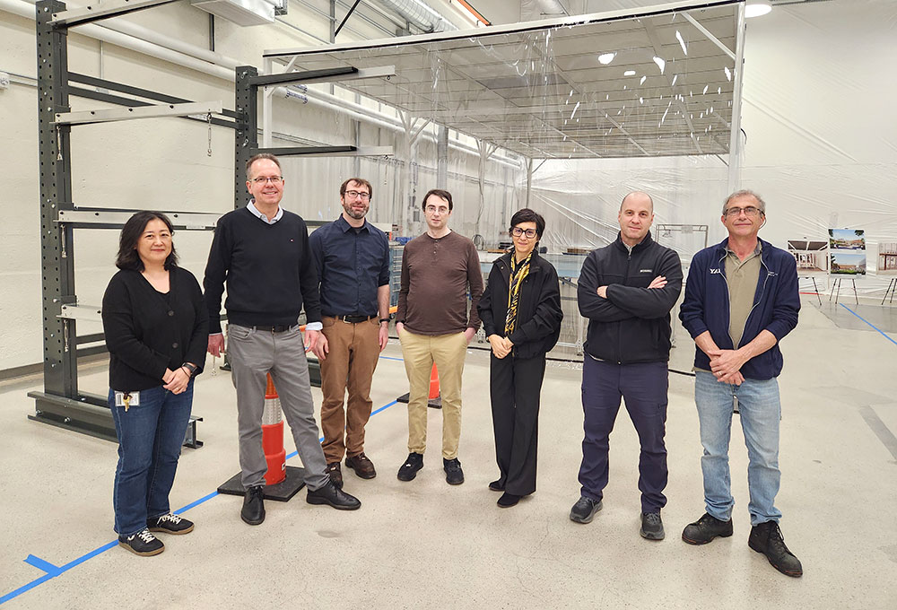 Seven people standing posing for a picture in front of the DUNE assembly setup at Wright Lab."\