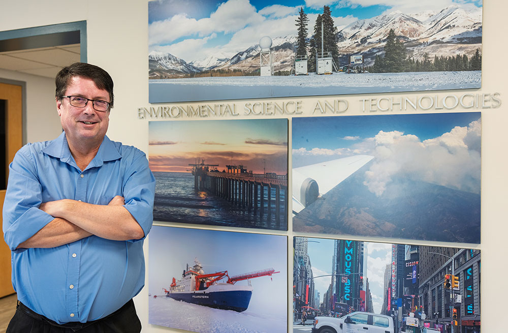 Mike Jensen stands near a wall of photos from research sites