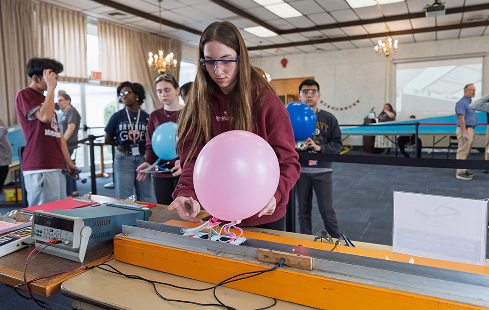 A student gently places her handmade Maglev vehicle, here affixed with a balloon, on a vertical magn