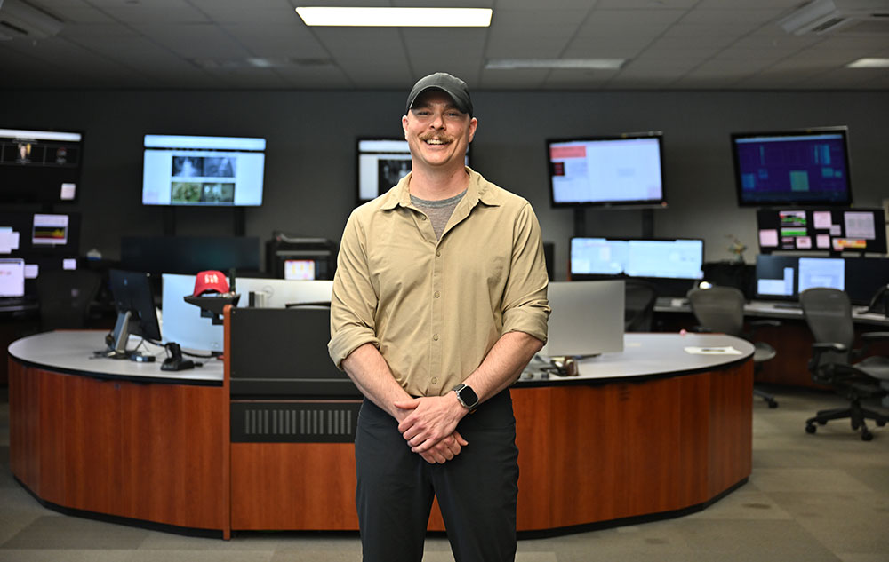 Jordan Ziegler stands in the Relativistic Heavy Ion Collider Main Control Room at Brookhaven Nationa