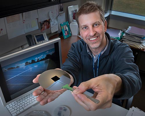 Charles Black holds a nanotextured square of silicon on top of an ordinary silicon wafer
