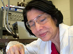 Triveni Rao, wearing clear safety goggles over her eye and a white lab coat with a Brookhaveb Lab lo