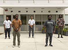 Students stand in a line in front of physics building