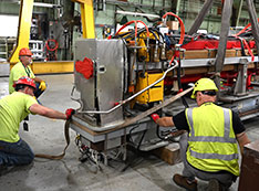 Technicians wearing hardhats and bright yellow shirts rig magnet