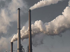 Clouds of emissions rise from smokestacks from a waterfront industrial complex.