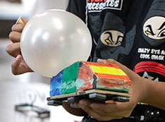 Student attaching a balloon to painted Styrofoam car