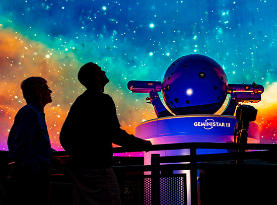 Silhoutte of two people looking up at a colorful night sky in the Reichert Planetarium