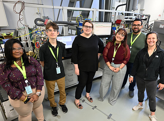 The photo angle is taken from slightly above. The four interns wear neon green lanyards around their