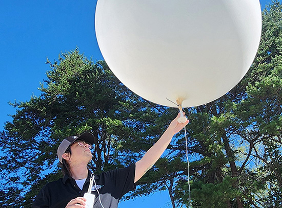 A person holds the bottom of a weather balloon with their left hand and a radiosonde in their right