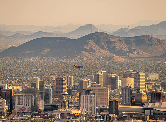 A plane flies over the downtown skyline of Phoenix, Arizona, with hot air balloons floating over dis