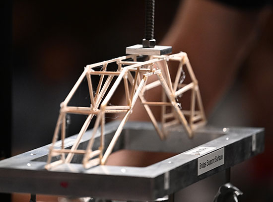 A wooden model bridge sits atop the metal frame of a crashing mahcine