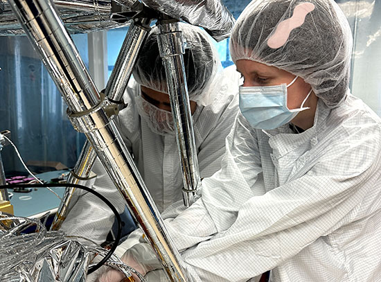 Engineers wearing clean room gear assemble machinery