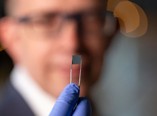 A chip held in tweezers by a man who is out of focus in the background.