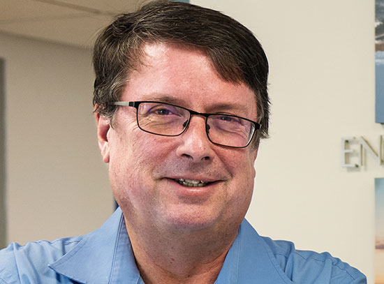 Mike Jensen stands near a wall of photos from research sites