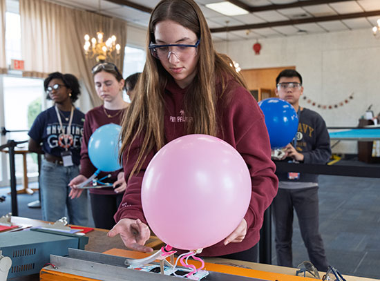 A student gently places her handmade Maglev vehicle, here affixed with a balloon, on a vertical magn