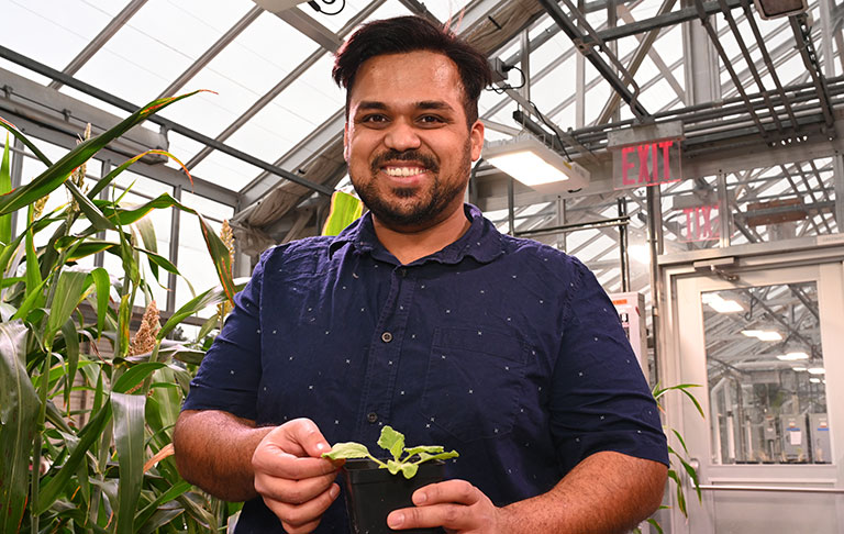 Sanket Anaokar holds a small green plant in a glass greenhouse