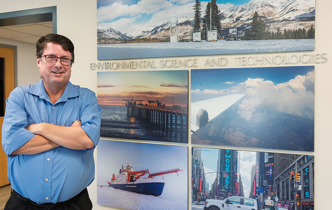 Mike Jensen stands near a wall of photos from research sites