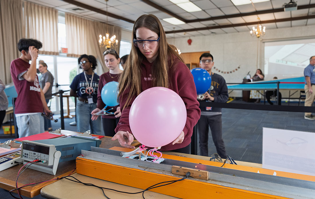 A student gently places her handmade Maglev vehicle, here affixed with a balloon, on a vertical magn